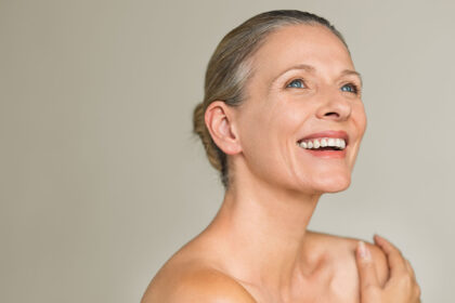 Portrait of a cheerful senior woman smiling while looking away isolated on gray background. Happy mature woman after spa massage and anti-aging treatment on face.