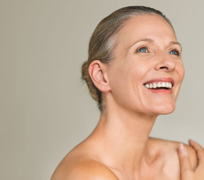 Portrait of a cheerful senior woman smiling while looking away isolated on gray background. Happy mature woman after spa massage and anti-aging treatment on face.